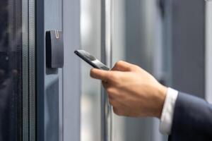 A person in a suit uses a smartphone near a door access system, possibly for security or entry. photo