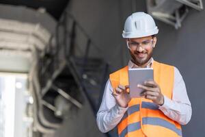 An engineer in safety gear smiles while using a tablet, inspecting a project on-site. Construction and technology integration. photo