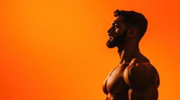 Strong man posing against a vibrant orange backdrop showcases muscular physique during a fitness photo session, emphasizing strength and determination in a gym environment