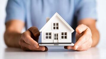 Miniature house held by person over smartphone showcasing digital real estate interaction in a modern setting photo