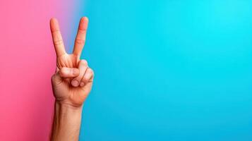 Hand gesture showing peace symbol against a bright blue and pink background during a vibrant creative event or social gathering highlighting positivity and goodwill photo
