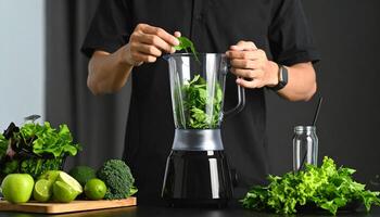 A person prepares a healthy green smoothie with fresh vegetables, fruit, and spinach in a blender for a nutritious drink. photo