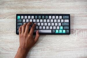 Overhead View of Person Typing on Teal and Gray Keyboard on Wooden Desk photo