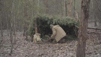 Winter bushcraft shelter built from pine branches in the forest, A man takes cover under a handmade pine shelter during snowfall in a quiet woodland video