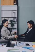 Two businesswomen shaking hands at an office desk photo