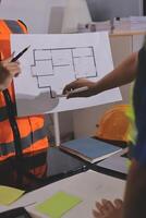 A man in an orange vest and safety vest is holding a blueprint photo