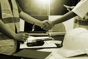 Two construction workers shaking hands over a desk photo