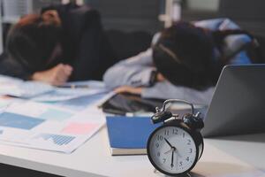 A woman sleeping on a desk with an alarm clock photo