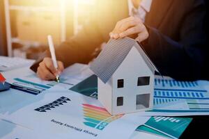 Businessman holding house model and financial report on table photo