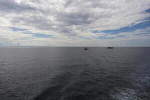 A boat is out in the ocean with a few clouds in the sky photo