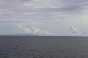 A boat is sailing across the ocean with a cloud in the sky photo