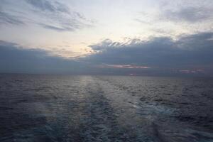 The sun sets over the ocean as seen from the back of a boat photo