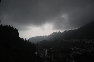 A dark sky over a town with trees and mountains photo