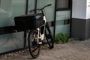 A delivery bicycle stands parked against a contemporary building. The photo