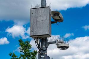 A concrete surveillance box sits on a tall pole alongside a camera and photo