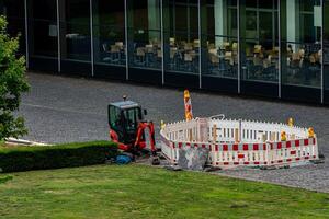 A small excavator works diligently near a fenced area being photo
