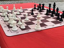 Outdoor chessboard setup with white and black chess pieces on red table background photo
