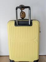 A bright yellow suitcase with sunglasses stands near a white wall. photo