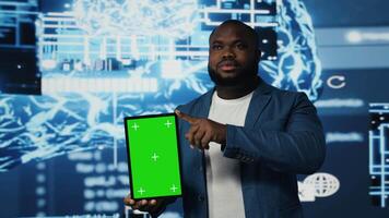 African american tech engineer reviews algorithmic data next to mockup, holding a tablet surrounded by digital visuals. AI smart technology and neural networks in a modern environment. Camera A. video