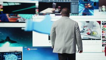 Man stands in front of digital videowall surrounded by streaming videos and social media clips. User instantly accessing thousands of entertainment options through multimedia dashboard, camera A