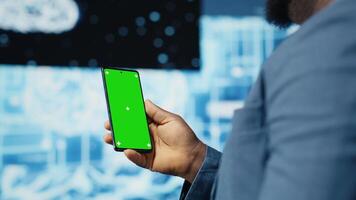 Focused black IT professional looks at phone with green screen, standing in a digital artificial intelligence environment. Solving deep learning tasks for big data automation. Cybernetics. Camera B. video