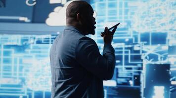 African american IT specialist calling a technician on his smartphone, talking about automation via neural networks systems. Businessman discuss about coding and data processing. Camera B. video