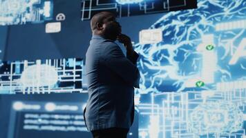 African American businessman studying digital AI brain interface, symbolizing neural networks, data science and algorithmic thinking. Cybernetics for a high tech futuristic innovation. Camera B. video