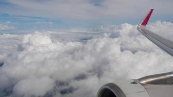 Scenic view of aircraft wing above the clouds, seen through the airplane window. Fluffy white clouds and clear blue sky create a peaceful and inspiring in-flight atmosphere video