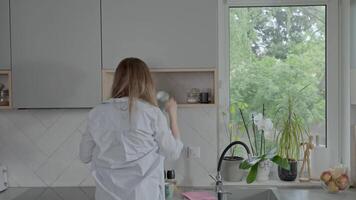 Woman clears an open kitchen shelf by removing mugs and jars. Tidy organization, and everyday routines concept video