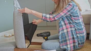 Woman using power drill to attach part to underside of chair during furniture assembly video