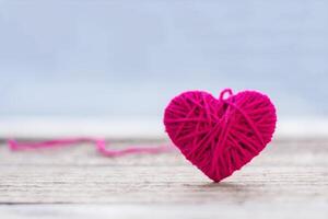 red knitting wool in shape of heart on vintage wooden with bokeh soft light background. photo