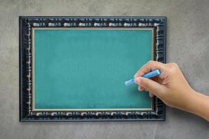 The hand that catches Chalk is preparing to write the alphabet on empty green chalkboard with black wooden frame on grunge cement wall, vintage wall texture background. photo