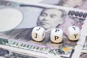 close-up of wooden cube with text J P Y on banknote YEN for business and financial concept. photo