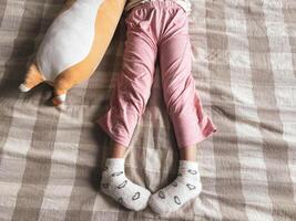 Legs of a girl about 5 years old and plush cat toys on the bed. The child plays on the bed. photo