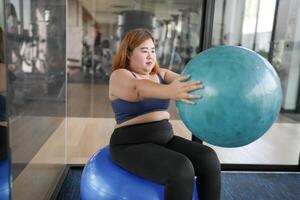 a obese woman is sitting on an exercise ball in a gym photo