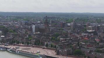 Aerial view of Nijmegen, Netherlands, featuring St. Stevenskerk, river cruise ships on the Waal River, moving vehicles, and lush greenery. video