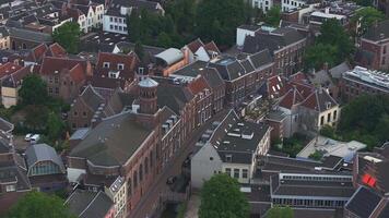 Aerial pan over Utrecht, Netherlands, showing traditional Dutch buildings, modern structures, narrow streets, and lush greenery in a quaint urban setting. video