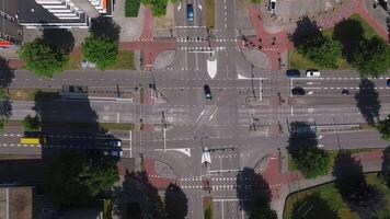 Aerial view of a busy intersection in Eindhoven with moving cars, bicycles, and pedestrians, surrounded by greenery, buildings, and parking spaces. video