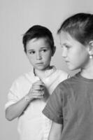 Close up black and white image of a small boy and girl facing each other, foreheads almost touching, gentle expressions, studio light highlights emotional connection. photo