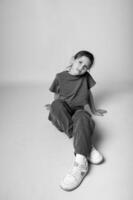 Full length black and white photo of a little girl posing like a model, one, neutral backdrop, strong contrast highlighting her pose and posture