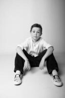 Monochrome image of a small boy standing in profile, light falling from one side, highlighting his eyelashes and delicate features. Minimalist studio backdrop. photo