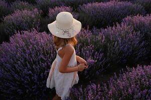 Back view of a girl in sunhat running through a lavender field at dusk. photo