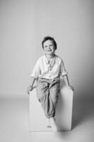 Black and white portrait of a toddler boy with tousled hair, sitting cross-legged on the floor, looking up with curiosity. Soft light wraps around him. photo