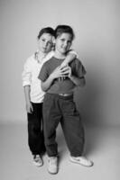 Monochrome full-length photo of a boy and girl standing slightly apart, looking at the camera with serious faces. Strong contrast and minimalist backdrop.