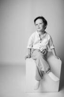 Stylized studio portrait of a quiet young boy leaning against a wall, eyes downcast, dramatic lighting creates strong shadows and emotional depth. photo