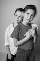 Tight black and white portrait of a young brother and sister, faces close together, looking in different directions. Studio lighting creates soft shadows and emotional depth. photo