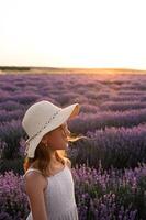 Kid in straw hat enjoying nature in lavender field during twilight. photo
