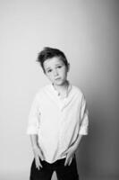 Black and white studio portrait of a young boy standing confidently, hands by his sides, looking straight at the camera. Clean background, simple lighting emphasizes form and presence. photo