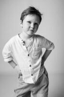 Studio shot of a smiling little boy in a white shirt, standing against a black background. High contrast enhances the joyful expression and sparkle in his eyes. photo