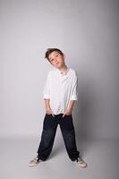 Monochrome image of a young boy standing barefoot on a plain backdrop, arms crossed, with a confident and slightly defiant look. Stark lighting adds depth and contrast. photo